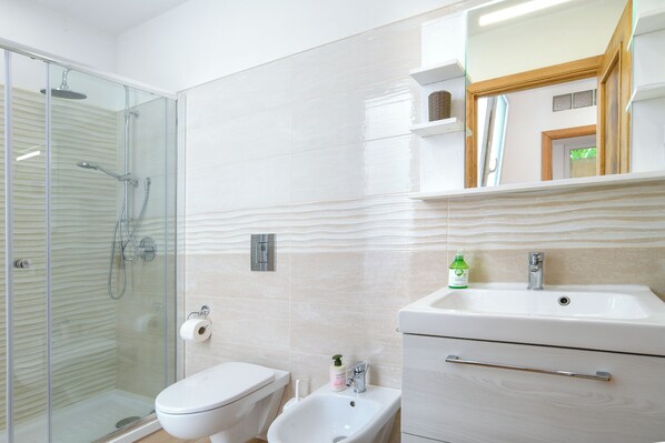 Une salle de bain dotée d’une douche à parois de verre, de toilettes, d’un bidet et d’un lavabo avec un miroir au-dessus.