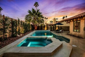 A swimming pool with a stone border, surrounded by palm trees and a sunset sky. - Paradise at Waring Place (Palm Desert)