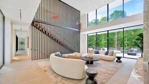 Ein modernes Wohnzimmer mit einer gebogenen weißen Couch, einem Couchtisch und einer Treppe mit Streifen-Geländer.