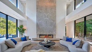 Ein modernes Wohnzimmer mit Kamin, zwei Sofas, einem Couchtisch und großen Fenstern.
