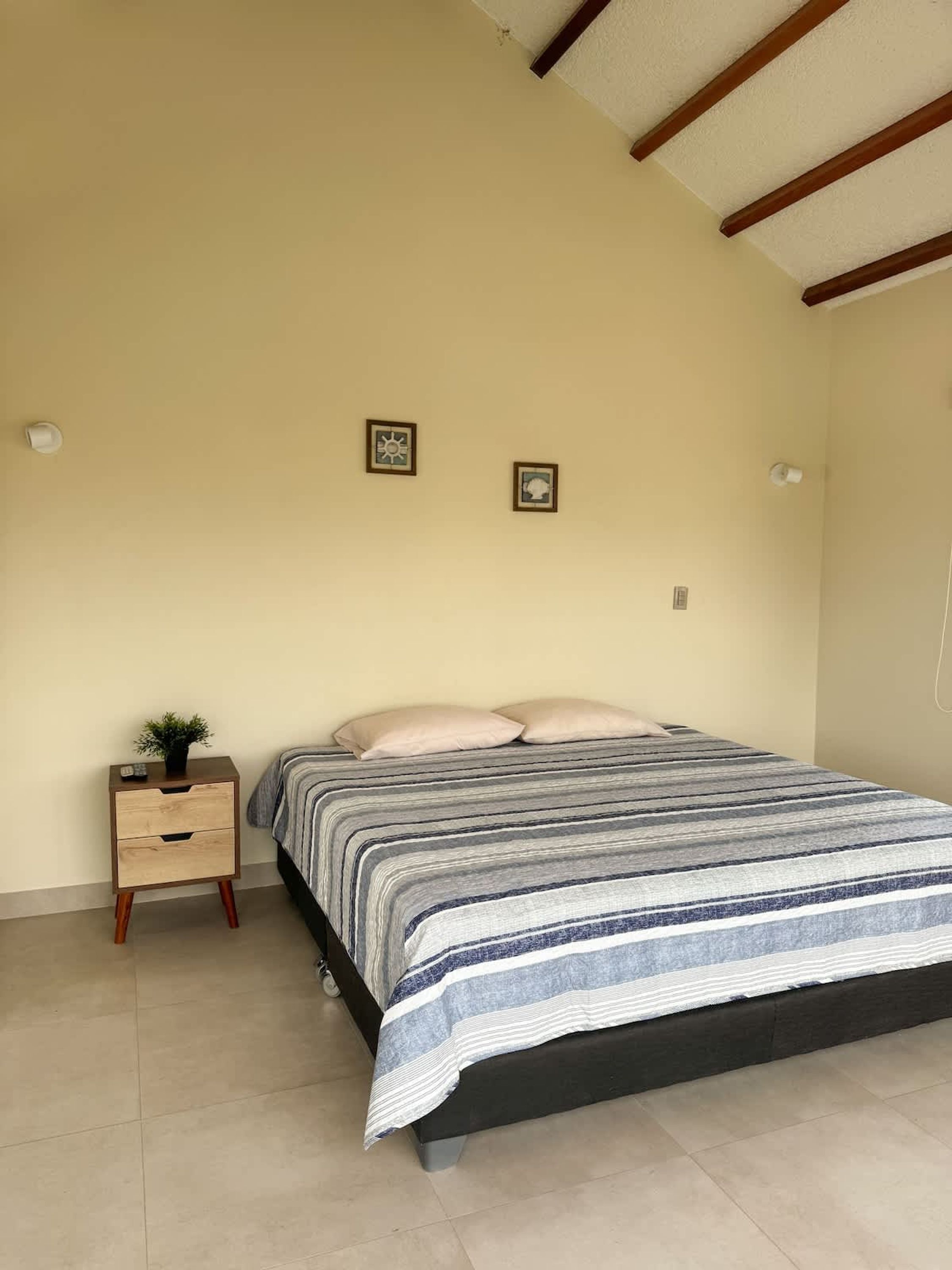 A bedroom with a bed, a nightstand with drawers, two wall-mounted light fixtures, and two framed pictures.