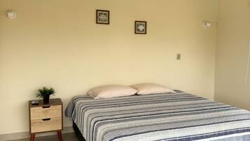 A bedroom with a bed, a nightstand with drawers, two wall-mounted light fixtures, and two framed pictures.