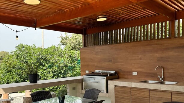 Cocina exterior con comedor, que incluye una mesa y sillas, y vistas a zonas verdes al fondo.