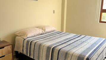 A bedroom with a bed, a nightstand, a painting on the wall, and a window.