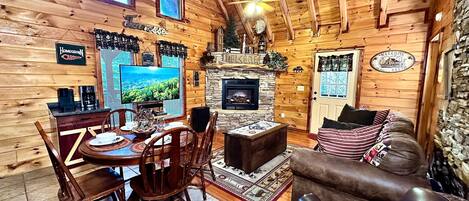 A cozy cabin interior with a dining area, a fireplace, and a living room with a couch.