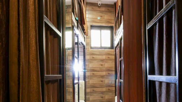 A narrow hallway with wooden walls and a tiled floor, leading to a room with a bed and a window. - Negasi Dormitory (Mumbai)