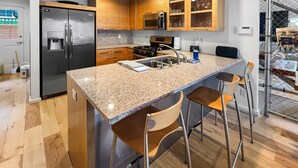 Eine moderne Küche mit Granit Arbeitsplatte, Edelstahlgeräten, Holzschränken und einer Bar mit Hockern.