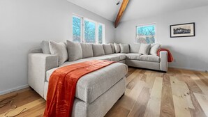 Ein modernes Wohnzimmer mit einer Eckcouch, großen Fenstern und einem Holzbalken an der Decke.