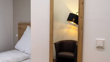 A bedroom with a wooden headboard bed, a large mirror, a chair, and a bedside lamp.