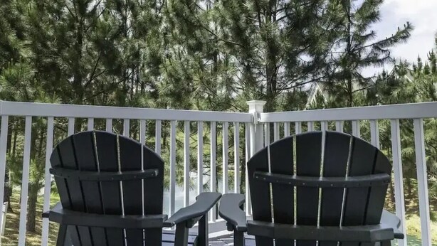 A deck with two Adirondack chairs facing a forest of tall pine trees. - The family -friendly resort life is waiting for you! 
 (Williamsburg)