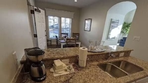A kitchen with granite countertops, a coffee maker, a toaster, a sink, and a dining area visible through an archway. - The family -friendly resort life is waiting for you! 
 (Williamsburg)