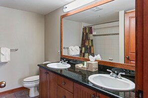 Ein Badezimmer mit zwei Waschbecken, einer Toilette, einem Spiegel und einer Duschvorhang.