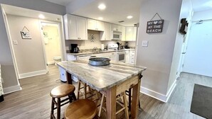 Una cocina con armarios blancos, encimera de mármol y taburetes de madera.