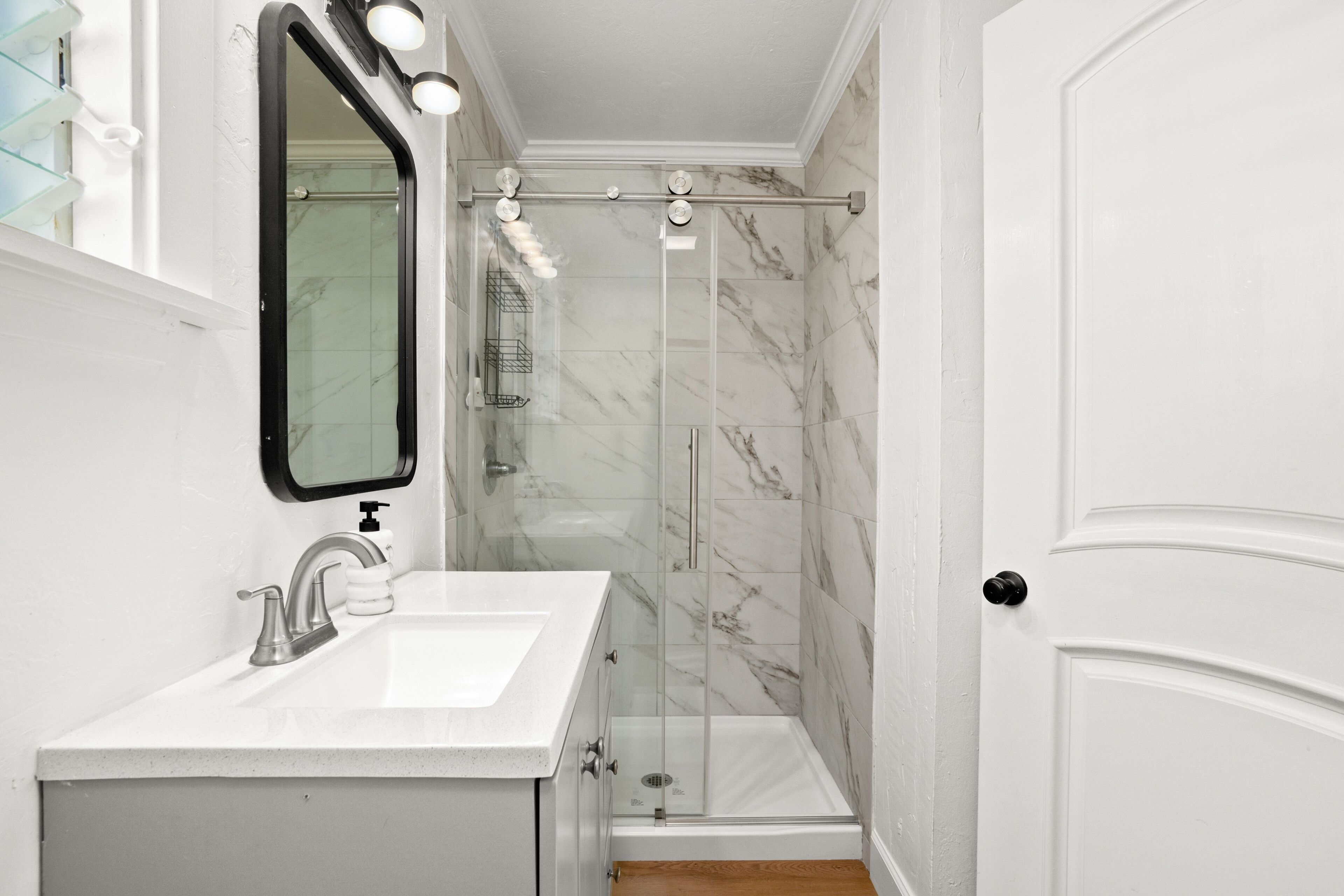 A bathroom with a white sink, mirror, and glass shower enclosure.