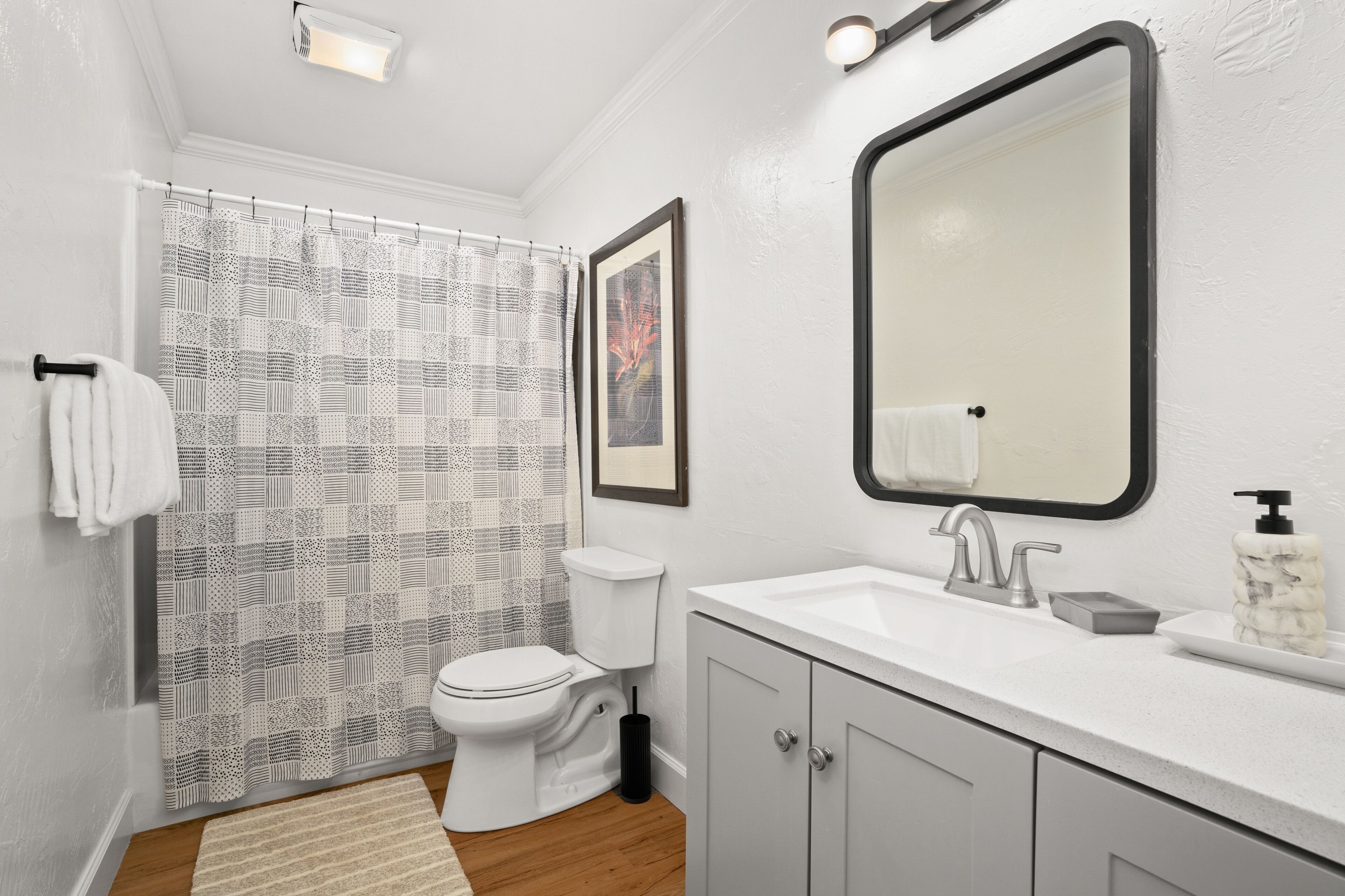 A bathroom with a toilet, sink, mirror, and patterned shower curtain.