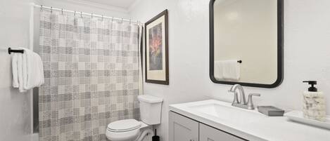 A bathroom with a toilet, sink, mirror, and patterned shower curtain.