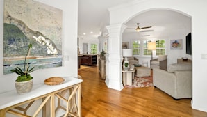 A spacious living area with a wooden floor, a white couch, a coffee table, and a dining area with a white table and chairs. - Kauai Wainani Villa 2 Bedroom Home (Koloa)
