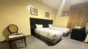 A hotel room with two beds, a desk, and a chair. There are framed pictures on the wall and a curtain on the window. - Orchida Al Hamra (Riyadh)