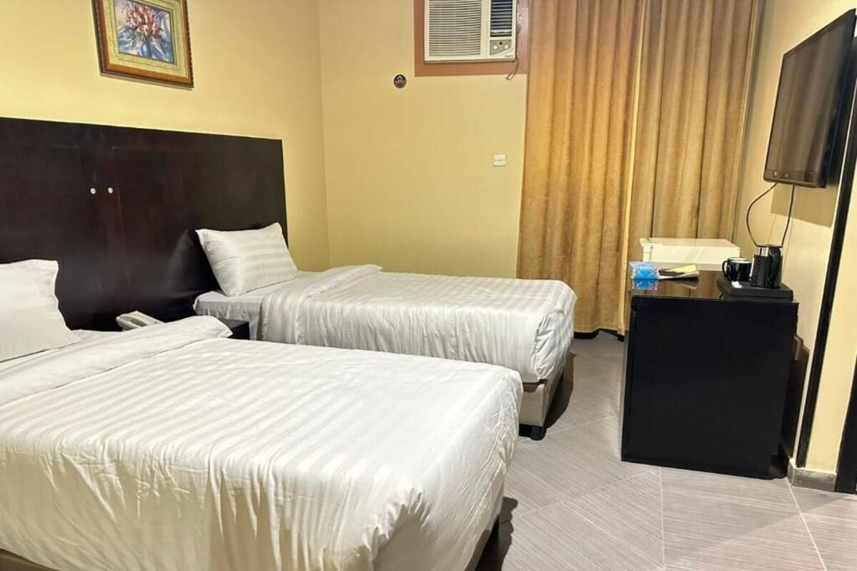 Habitación de hotel con dos camas, un escritorio, un televisor y una ventana con cortinas.