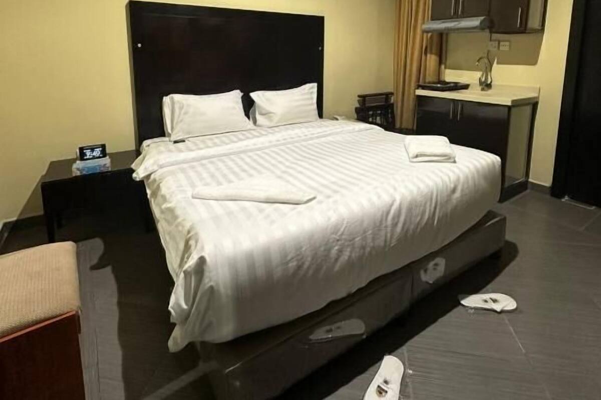 Habitación de hotel con una cama grande, una mesita de noche, un escritorio pequeño, una silla, un armario y un equipo de aire acondicionado.