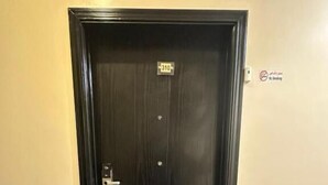 A dark wooden door with a numeric keypad lock, a small sign above it, and a no-smoking sign on the wall to the right. - Orchida Al Hamra (Riyadh)