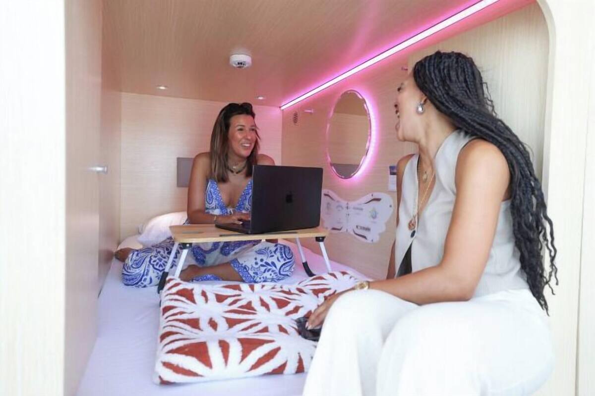 A modern room with a bed, a laptop on a small table, and a mirror on the wall.