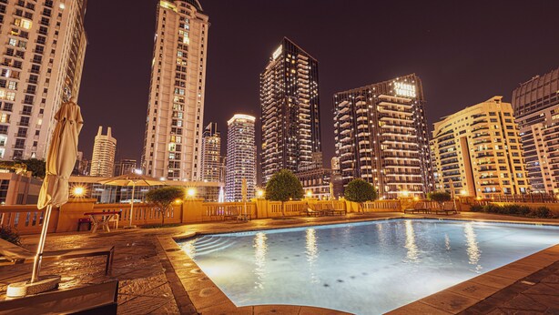 Vista notturna di una zona piscina con alti edifici sullo sfondo.