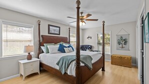 Un lit à baldaquin avec un ventilateur de plafond, une table de chevet avec une lampe et une commode en osier.