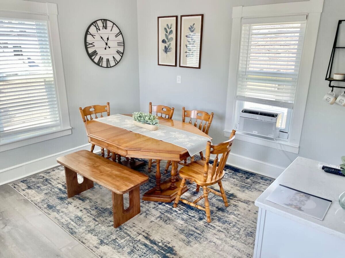 A dining room with a wooden table and chairs, a clock, and framed artwork on the wall.