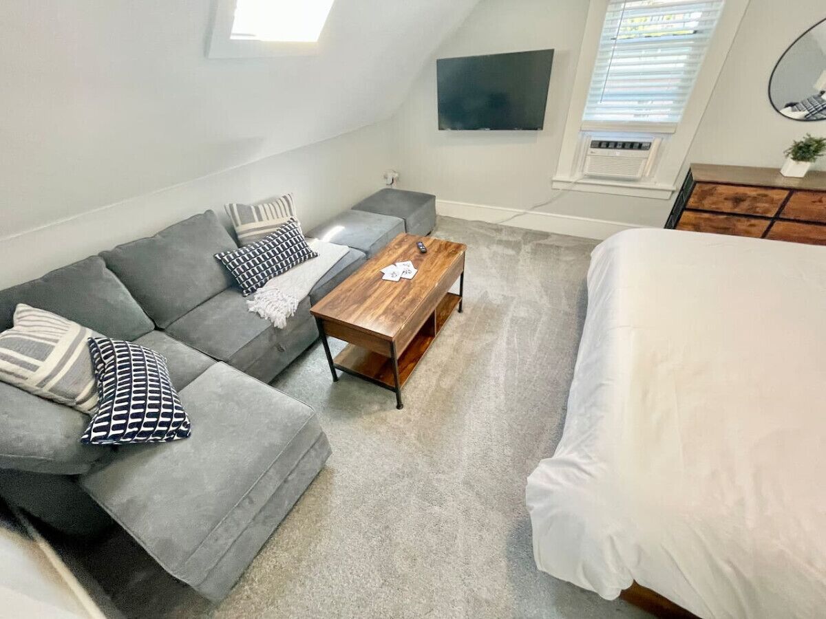 Une chambre moderne avec un canapé gris, une table basse en bois et un lit avec une literie blanche.