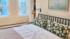 Une chambre à coucher avec un lit, une fenêtre, une lampe fixée au mur et un tableau.