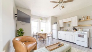 Eine moderne Küche mit weißen Schränken, einem eingebauten Backofen und einer Mikrowelle. Ein Esstisch mit Stühlen und ein Deckenventilator sind vorhanden.