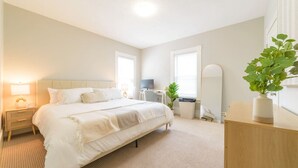 Ein Schlafzimmer mit einem großen Bett, Nachttischen, einem Schreibtisch, einem Stuhl, einem Fernseher und einer Pflanze.