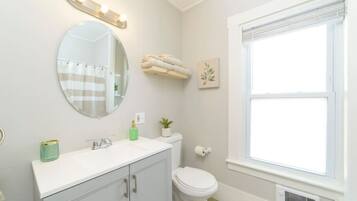 A bathroom with a round mirror, a white sink, a toilet, and a window.
