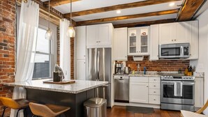 A kitchen with white cabinets, stainless steel appliances, and a brick wall. - Tugboat Vista 2 Bedroom Downtown Portsmouth (Portsmouth)