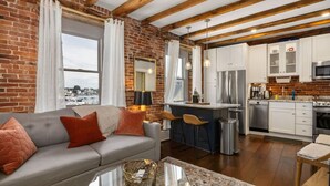 A modern kitchen with white cabinets, stainless steel appliances, and a brick wall. - Tugboat Vista 2 Bedroom Downtown Portsmouth (Portsmouth)