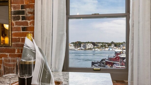 A hotel room with a large window overlooking a harbor, a marble table, and a bottle of champagne. - Tugboat Vista 2 Bedroom Downtown Portsmouth (Portsmouth)