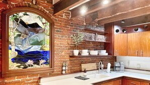 Una cocina con pared de ladrillo, armarios de madera, encimera blanca y una ventana de vitral.