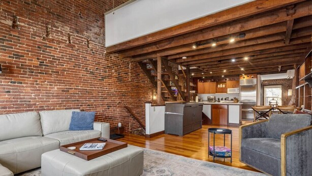 Un loft amplio con vigas de madera a la vista, pared de ladrillo y cocina equipada con electrodomésticos modernos.
