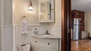Un baño con tocador blanco, aro para toallas, espejo y lámpara.