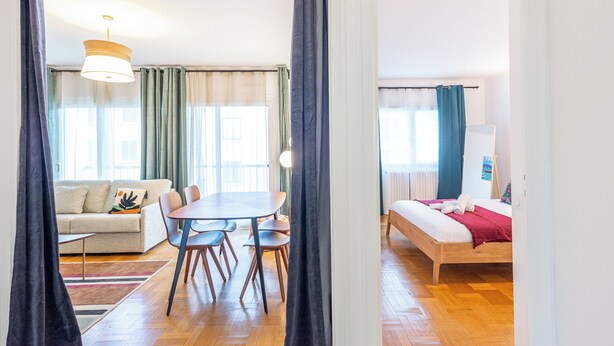 Et moderne værelse med trægulv, et spisebord med stole, en sofa og en seng med rødt tæppe.