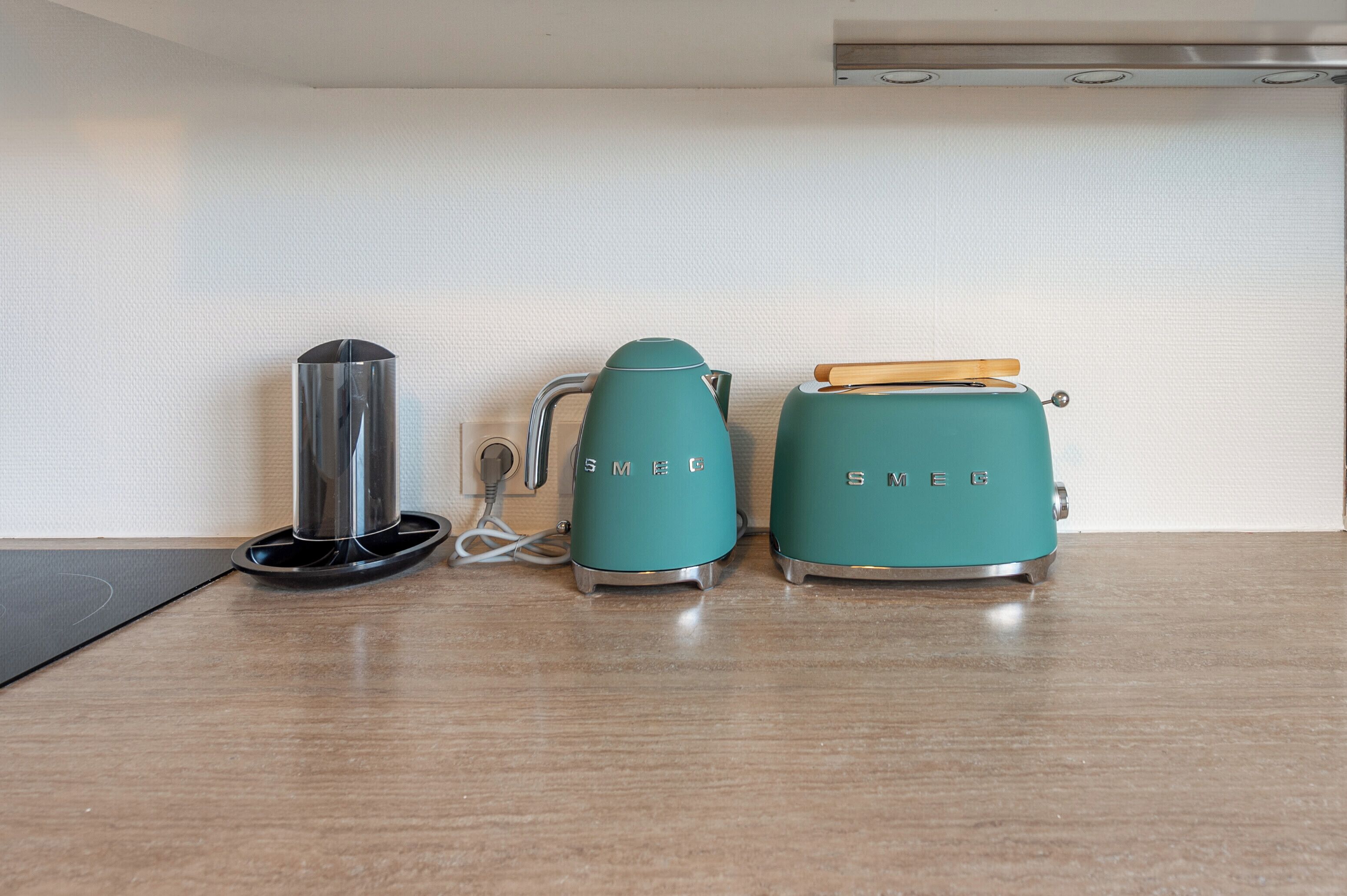 Et køkken med en elkedel i rustfrit stål, en elkedel i turkis og en turkis toaster på en træbordplade.