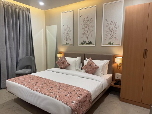 A neatly arranged hotel room with a large bed, a chair, a wardrobe, and two wall-mounted lamps. - Hotel Aura By Arihant (Udaipur)
