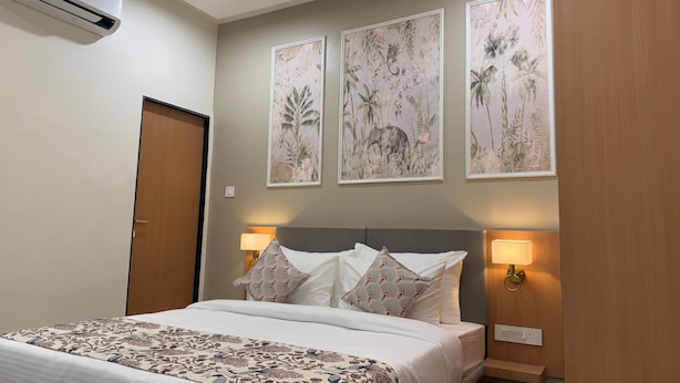 A hotel room with a bed, a nightstand, wall-mounted lamps, and three framed botanical prints. - Hotel Aura By Arihant (Udaipur)