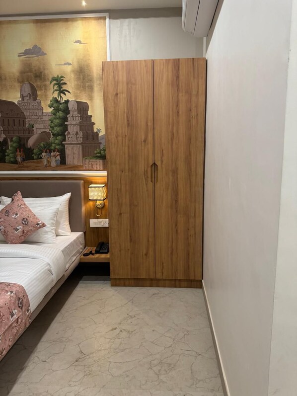 A bedroom with a bed, a wooden wardrobe, a nightstand, and a wall mural. - Hotel Aura By Arihant (Udaipur)