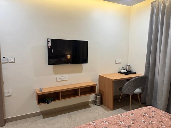 A small, modern room with a bed, a desk, a chair, a TV, and a shelf.