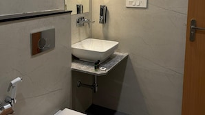 A modern bathroom with a white sink, mirror, and toilet. - Hotel Aura By Arihant (Udaipur)