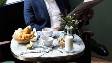 A breakfast setting with croissants, coffee, milk, and a newspaper on a marble table.