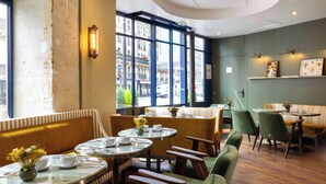 A restaurant with round tables, green chairs, and a view of buildings through large windows. - Les Rives Oceanik (Paris)
