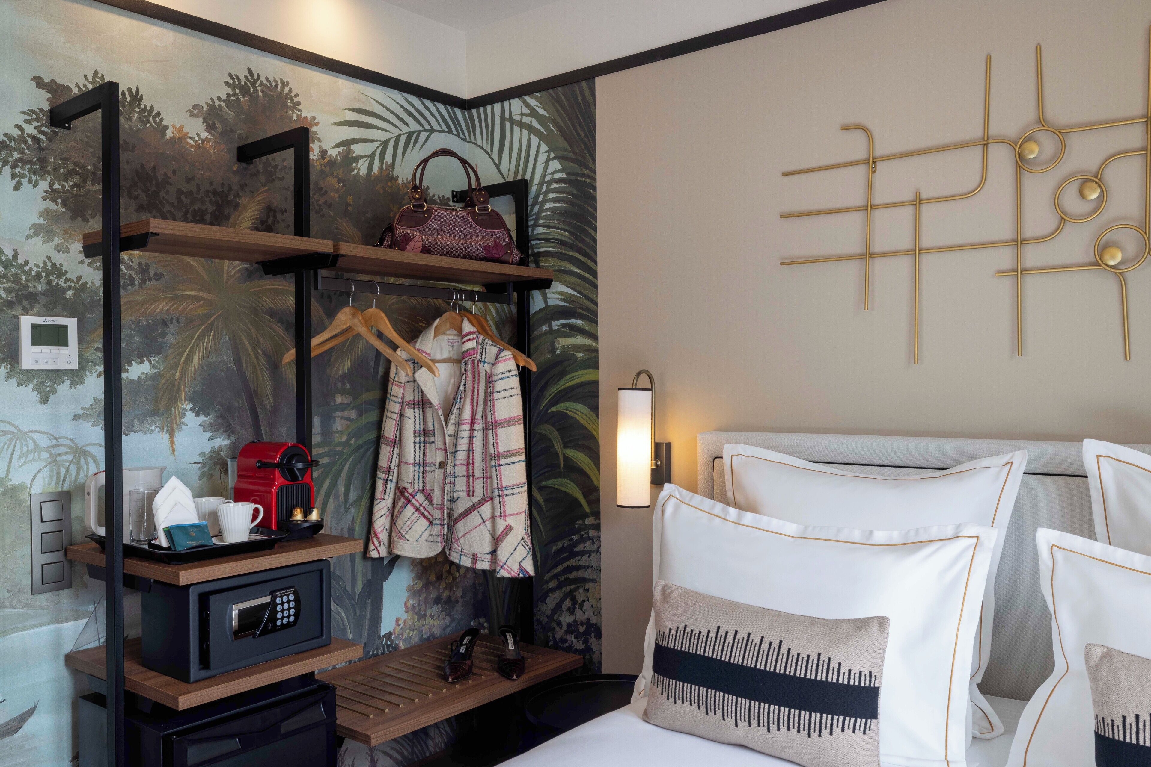 Ein Hotelzimmer mit einem Bett, einem Nachttisch mit Lampe, einem an der Wand befestigten Regal mit einer Handtasche und einer Wand mit dekorativem Design.